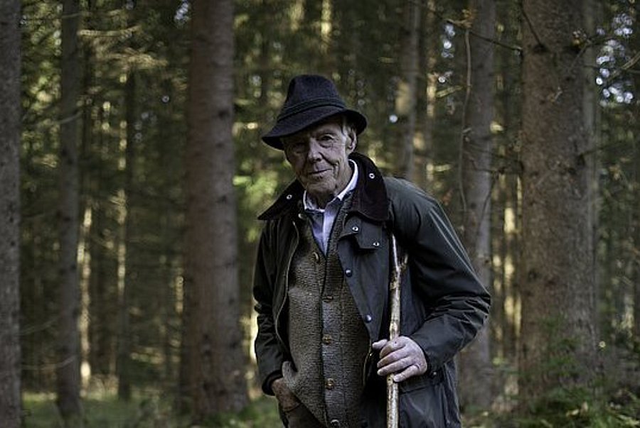 Josef Göppel steht im Wald, nehmen ihm sitzt sein Jagdhund Akso.